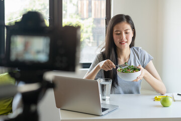 Social media and content creator occupation new job in future. beauty asian blogger eating fresh homemade salad breakfast and recording video for online channel live.