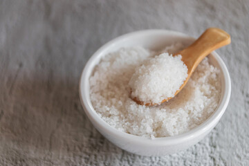 Fototapeta na wymiar Flower of salt on wooden spoon in white bowl (Fleur de sel) is a salt that forms as a thin, delicate crust on the surface of seawater as it evaporates.