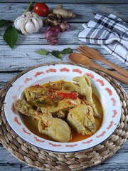 Image of spicy chicken curry or kare or kari or gulai ayam, an indonesian traditional cuisine. Served in enamel bowl over wicker placemat on white wooden kitchen table. Some ingredients appeared. 