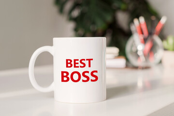 Coffee mug with text BEST BOSS in workplace background.