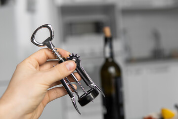 Metal corkscrew in a man's hand with a bottle of red wine on a background with a light white...