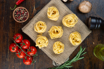 Raw pasta tagliatelle with fresh tomatoes, peppers, asparagus beans, spices and cheese on a wood table.