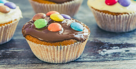 close up of a muffin with coating and chocolate lentils againt wooden background