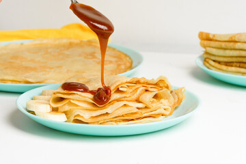 blini pancakes with caramel, dripping on a spoon levitation close-up on a blue plate on a light...