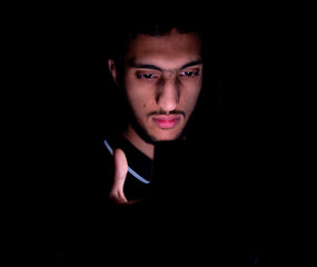 Portrait of middle eastern guy checking his phone in a dark room