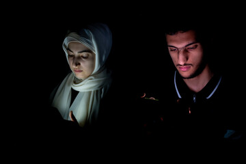 portrait of middle eastern guy and girl using their phone in a dark room