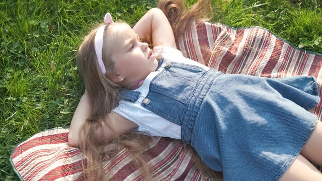 Pretty little child girl with closed eyes laying down on blanket on green grass in summer taking a nap.