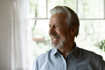 Happy senior 70s aged man looking away and laughing at funny joke. Healthy mature older person having fun at home, enjoying retirement, having great health, getting good news. Elderly OAP age concept