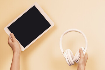Online learning, remote education, e-learning concept. Hands holding digital tablet and wireless headphones over pastel color background