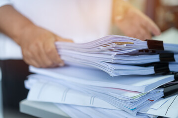 Employee checking business unfinished documents with stacks paper files and managing document achieves preparing meeting planing at busy work in financial office. Tax time in filing information - obrazy, fototapety, plakaty