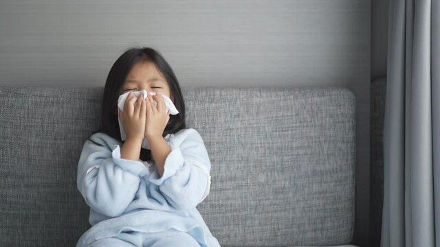 Asian child or kid girl sick and sneezing on nose with cold cough on tissue paper from influenza coronavirus and allergy weak or virus bacteria from PM 2.5 dust weather or smoke at hospital or home