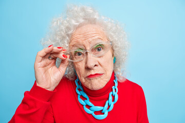 Portrait of beautiful wrinkled senior woman has curly grey hair bright makeup manicure looks...