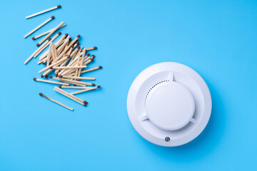 A pile of matches and a fire detector on a blue background. Fire safety concept.
