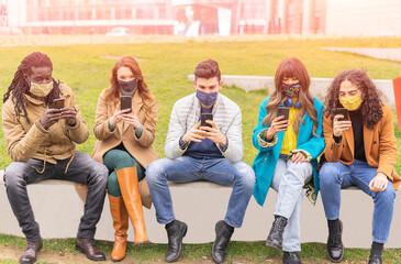 Obraz premium Group of trendy friends wearing face safety masks while watching videos on smartphone - Concept of new normal , technology and covid-19