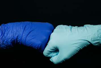 The two person bumping fists together (in protective gloves) on black background. A symbolic form of greeting-hello in the time of the coronavirus pandemic.