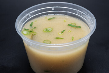Bowl of Miso soup shows delicious cloudy broth containing green onion, seaweed, and spicy flavor in clear container.