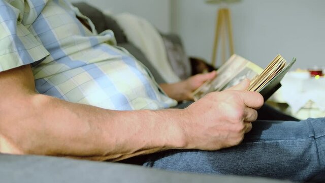 elderly man looks through album with old photographs of 1960-1970, concept of family tree, genealogy, memories of youth, childhood, remembering his life, relatives, family connection of generations