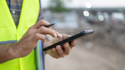 Close up construction worker holding pen touch screen using smartphone construction site outdoor