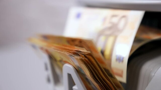 Euro currency on counting machine. 50 euro banknotes counting in the machine. Counting mechanism is processing euros. Female hand taking money. Close-up.