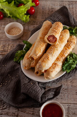 Sausages in the dough - filo with sesame seeds on a wooden gray background with greens and cherry
