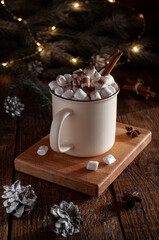 Christmas cocoa with marshmallow and cinnamon stick in a light large mug on the background of a fir tree with a garland
