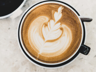 Top view of hot coffee latte foam of flower design art on beige marble table in cafe. Drink and beverage.
