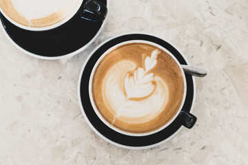 Top view of hot coffee latte foam of flower design art on beige marble table in cafe. Drink and beverage.