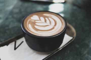 Black ceramic cup of hot coffee latte foam design art on the tray on green marble table. Barista craft.