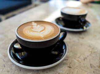 Black cup of hot coffee latte foam of flower design art on beige marble table in cafe. Drink and beverage.