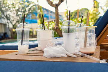 Used empty plastic cups with straws on wooden table near sun bed. Beverages delivery concept.