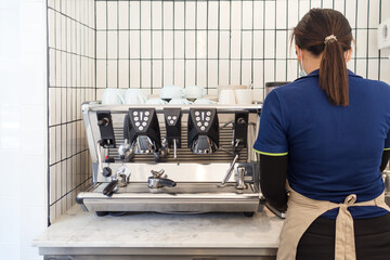 Female Barista in protective mask is standing and making coffee by using coffee machine at cafe.