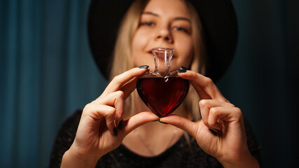 Cropped image of woman holding heart shaped glass jar of love potion. Beautiful young woman in a...