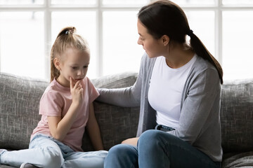 Serious mother talking to sad upset preschooler daughter kid at home. Mum consoling quiet girl,...