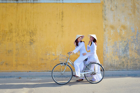 Two beautiful Asian women riding a bicycle in the city, Hoi An, Vietnam
