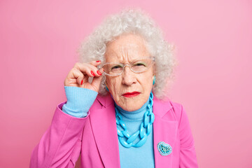 Portrait of scrupulous granny has attentive gaze at camera bad eyesight keeps hand on rim of...