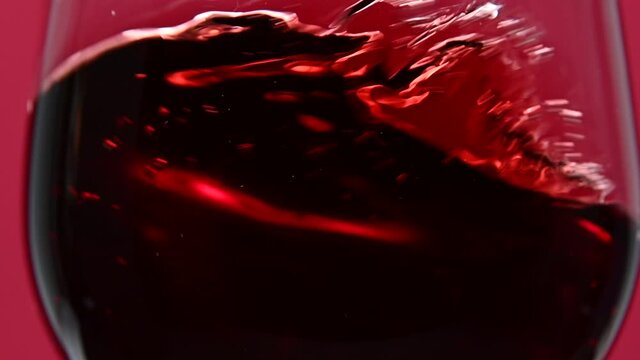 Close up swirling red wine in wineglass over red