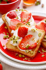 Toasts with fresh strawberries, creamy cheese and pistachios on a ceramic plate, close-up. An idea for a delicious breakfast or dessert.