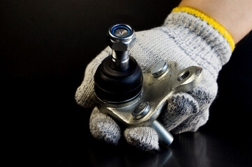 Brand new ball joint car on a black background in the hand of a mechanic in a glove. The ball joint...