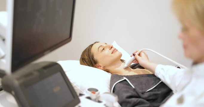 Doctor examining thyroid of female patient with ultrasound scan in medical spa. Concept of ultrasound examination and health checkup