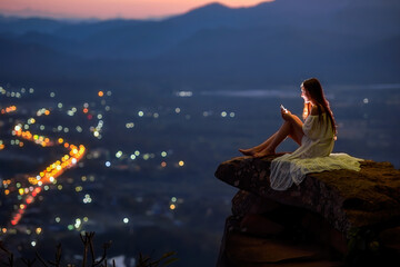 Woman sitting on a ledge above city using a mobile phone, Thailand