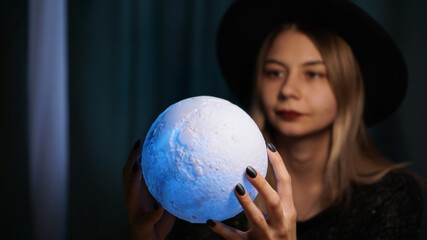 A young woman fortune teller in a hat is holding a magic ball. Beautiful psychic woman is guessing with a blue magic ball