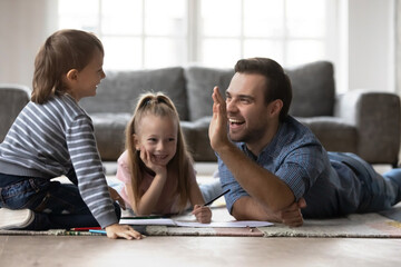 Best dad gives high five to happy little kid, plays and draws on heating floor. Father enjoys...