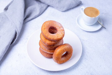 Donuts with powdered sugar and a cup of coffee. Traditional donuts in the shape of a ring fried in oil. Unhealthy but tasty food. Close-up, light background.