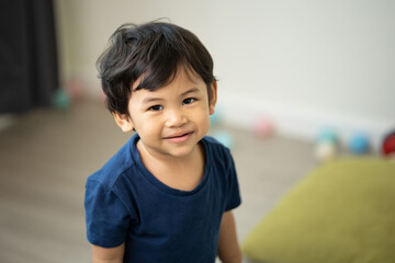 An Asian boy about 1 year old. Play in the living room of the house. He is wearing a blue shirt.