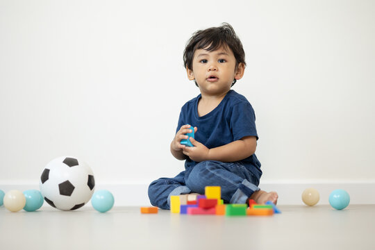 An Asian boy about 1 year old. Playing in the living room in the house He plays wooden toys in different colors. He is wearing a blue shirt.