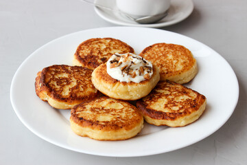 Breakfast of cheesecakes on a plate with sour cream.