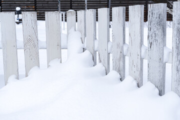 White vintage wooden fence above the middle covered with snow in winter