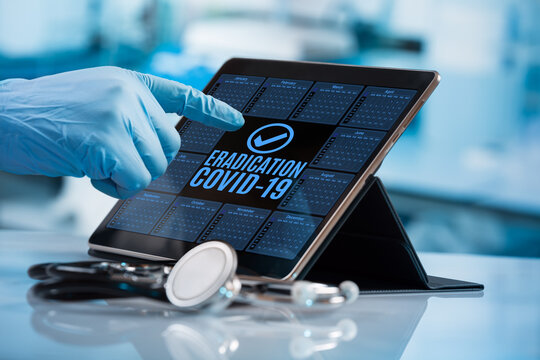 Doctor touching the screen of an electronic diary with the message covid-19 eradication. Doctor working with tablet in calendar of the pandemic vaccine plan for eradication of Coronavirus