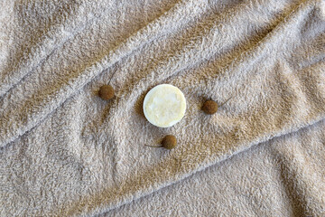 Spa accessories - round natural handmade soap and seeds of sycamore tree on beige fluffy terry towel. Hygiene, body care, health and wellness concept. Top view, flat lay. Selective focus. Copy space.