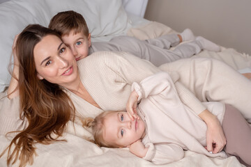 Fototapeta na wymiar Portrait of a happy mother and her two children son and daughter lying on a bed. Close up